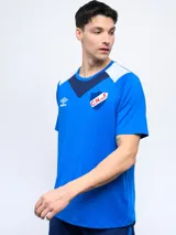 Remera de fútbol Umbro del Club Nacional de Football, modelo de entrenamiento. Diseño azul con detalles en blanco y rojo en cuello y mangas. Incluye logo de Umbro y escudo del club en el frente.