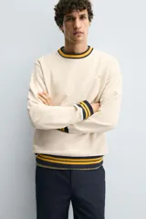 Sudadera color crema de corte regular fit, cuello redondo y manga larga. Presenta ribete a rayas en cuello, puños y bajo. Tiene un pequeño bordado de una flor en el pecho.