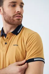 Remera tipo polo color ocre, de corte clásico, con cuello y mangas con terminaciones a contratono en azul marino y blanco.