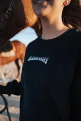 Buzo negro de manga larga con estampa en la espalda con una foto en blanco y negro de una ola y el logo de la marca Glassy.