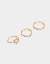 Set de tres anillos dorados con diferentes diseños: uno con forma de corazón calado, otro con eslabones entrelazados y otro con pequeñas esferas.