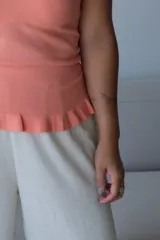 Musculosa de tejido de punto color coral, con escote en V, tirantes anchos y detalle de volado en el ruedo.