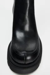 Bota negra de caña alta con suela track y tacón cuadrado. Cierre mediante cremallera lateral y tirador trasero.