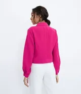 Campera color fucsia de crepe con cuello de camisa, manga abullonada, cierre frontal con botones y bolsillos frontales aplicados.
