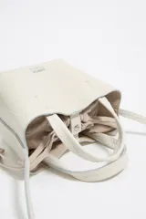 Bolso de mano mini de piel vacuna color blanco roto, con textura granulada. Presenta asas superiores y cordones ajustables laterales. El logo metálico de Bimba y Lola está grabado en el frente.