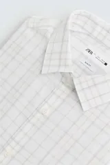 Camisa blanca con estampado de cuadros en tonos grises y amarillos, de corte regular fit, cuello italiano, manga larga con puños abotonados y cierre frontal con botones.