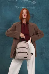 Mochila funcional color beige con detalles en negro, que incluye dos compartimentos con cierre y un bolsillo frontal para fácil acceso.