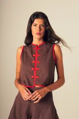Top marrón con ribetes rojos, sin mangas y cierre frontal con botones de nudo.