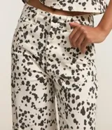 Pantalón wide leg de sarga con estampado animal print dálmata, trabillas en la cintura, cierre con botón y cremallera, y bolsillos delanteros y traseros.