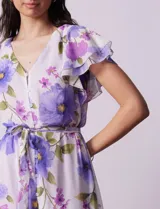 Vestido midi de gasa estampada con flores violetas y verdes, escote en V, abertura central con botones, cintura con lazo de ajuste y forro interno a tono.
