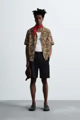 Camisa marrón con estampado floral, corte relaxed fit, cuello bowling, manga corta, bolsillo en el pecho, aberturas laterales y cierre con botones.