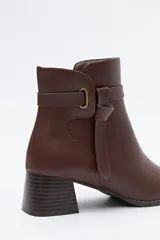 Bota corta de caña baja color negro, con puntera cuadrada, taco medio y tira decorativa con hebilla metálica en el lateral.