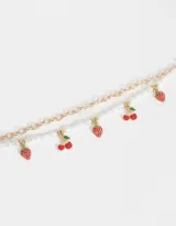 Set de dos pulseras: una de cadena dorada con dijes de frutilla y cereza, y otra de perlas sintéticas.