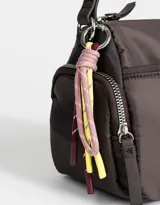 Bandolera de tela deportiva color lila, con correa regulable, bolsillo frontal con cierre, bolsillos laterales con cierre y charm decorativo.