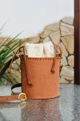 Cartera tipo canasta color marrón con textura simil cuero de cocodrilo. Tiene un forro interno de tela color crudo que se cierra con cordón. La correa es removible.