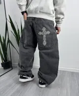 Pantalón de jean gris oscuro, corte holgado, con bolsillos delanteros y traseros. Presenta un bordado de una cruz ornamentada en el bolsillo trasero derecho.