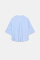 Camisa de lino color celeste claro, con cuello solapa, escote pico, manga corta con vuelta y dos bolsillos de plastrón en el delantero. Cierre frontal con botones.