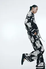Pantalón de sarga suave con estampado floral en blanco y negro, tiro alto, cintura elástica con cordón ajustable, piernas rectas con puño en el bajo y detalle de doble línea blanca en el ruedo.