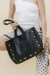 Bolso tote de cuero color marrón con tachas plateadas en los laterales. Tiene doble asa de hombro y un sobre interior de cuero.