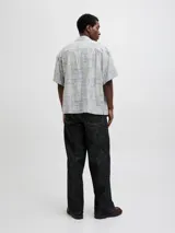 Camisa de manga corta Jack & Jones con cuello resort y calce amplio. Presenta un estampado integral de motivos náuticos y abstractos en tonos azul chambray y beige. Confeccionada en una mezcla de viscosa y lino, ideal para climas cálidos.