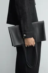 Bolso tipo shopper fabricado en cuero negro. Tiene un bolsillo interior plano con cierre mediante cremallera y asas de cuero.