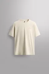 Camiseta color crema de corte holgado, cuello redondo y manga corta. Presenta un pequeño estampado con texto en el lado izquierdo del pecho.