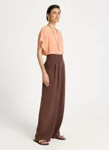 Pantalón sastrero marrón de pierna ancha, tiro alto, pretina estructurada con trabillas, pliegues frontales y cierre de cremallera.