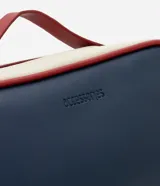 Neceser tipo baúl con dos compartimentos cerrados con cremallera, asa superior y tiradores. Diseño liso en azul marino y blanco con detalles en rojo.