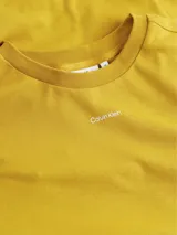 Remera color mostaza de corte holgado, con cuello redondo y logo de Calvin Klein estampado en el pecho.