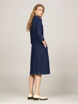 Vestido camisero midi de denim azul oscuro, con cuello clásico, manga tres cuartos y cierre frontal con botones. Incluye cinturón de la misma tela para ajustar a la cintura y dos bolsillos de parche con solapa en el pecho.