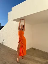 Vestido largo naranja de crepé con escote halter y falda tipo pareo con abertura lateral.