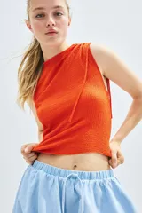 Top naranja sin mangas, de punto texturizado con escote bote y cordones ajustables en un lateral y en un hombro para crear un efecto drapeado.