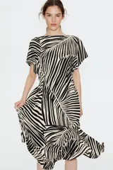 Vestido largo de punto con textura, estampado con motivos de hojas en blanco y negro. Tiene mangas cortas amplias, escote redondo y cintura entallada con pliegues.