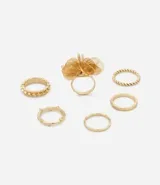 Set de seis anillos dorados de metal con diferentes diseños: uno con forma de flor, uno con textura trenzada, uno con textura de bolitas, uno con textura labrada, uno liso y uno con forma de rama.