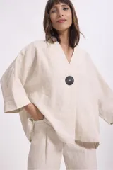 Blusa color crema de lino, de corte holgado, con cuello en V, mangas anchas y un botón grande negro.