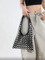 Bolso tipo tote de cuero sintético color borgoña, con apliques metálicos plateados y asa corta.