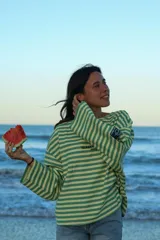 Buzo de manga larga con cuello redondo, reversible. Un lado es a rayas horizontales verde claro y verde oscuro, y el otro lado es liso verde oscuro. Presenta un estampado en la espalda con un logo de rayo y texto.