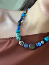 Collar corto con cuentas de madera, cristales checos y piedras naturales en tonos azules, marrones y turquesas. Se cierra con cadena de acero quirúrgico y gancho para regular el largo.