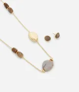 Conjunto de bisutería compuesto por un maxi collar asimétrico y un par de caravanas tipo botón. El collar presenta una cadena fina con baño dorado y diversas cuentas que imitan piedras naturales en variados formatos y tonalidades marrones y grises. Las caravanas son circulares con un diseño a juego inspirado en texturas minerales.