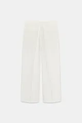 Pantalón marrón de tiro alto con bolsillos delanteros y falsos bolsillos traseros con tapeta. Detalle de pliegues en la parte delantera. Cierre frontal con cremallera y gancho metálico.