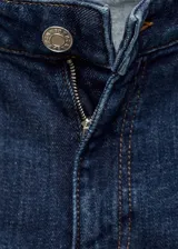 Pantalón de jean acampanado de tiro medio, color azul oscuro, con cinco bolsillos y cierre frontal con cremallera y botón.