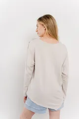 Remera color beige de corte holgado, con mangas largas, cuello redondo y bolsillo en el pecho. Presenta detalle de botones en el hombro.