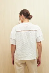 Camisa blanca de algodón liviano con diseño calado, cuello mao, mangas cortas abullonadas y detalle de pasamanería en el frente.