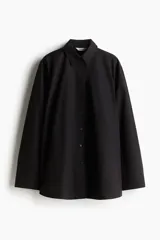Camisa negra oversized de algodón con cuello clásico, abotonadura frontal, mangas largas con hombros caídos, puños con abertura y bajo recto.
