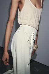 Pantalón de tiro alto color crema, de corte palazzo, con cinturón ancho de tela con hebilla metálica.