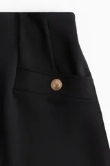 Short negro de tiro alto en punto interlock pesado con elástico oculto en la cintura y pinzas moldeadoras. Presenta bolsillos delanteros decorativos con botón de metal dorado.