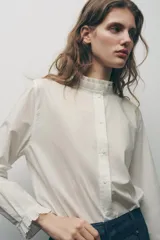 Camisa blanca de algodón con cuello con volantes y mangas largas con puños fruncidos.