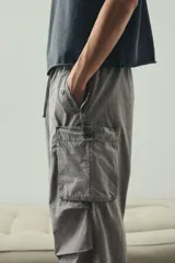 Pantalón cargo de algodón color gris claro, con corte holgado y cintura elástica ajustable con cordón. Presenta bolsillos cargo grandes en las piernas, pliegues cosidos en las rodillas y cordones ajustables en los bajos.