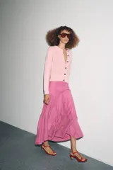 Chaqueta de punto color rosa pálido, con cuello redondo y cierre frontal de botones oscuros. Presenta mangas largas y un corte a la cintura.