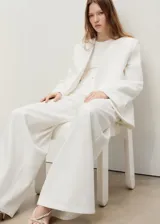 Pantalón de jeans blanco, tiro alto, corte wideleg (pierna ancha) y largo completo. Presenta cinco bolsillos y cierre frontal con botón y cremallera.